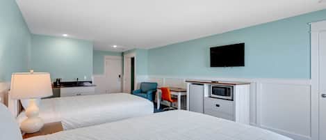 A hotel room with two beds, a desk, a chair, a TV, and a kitchenette.