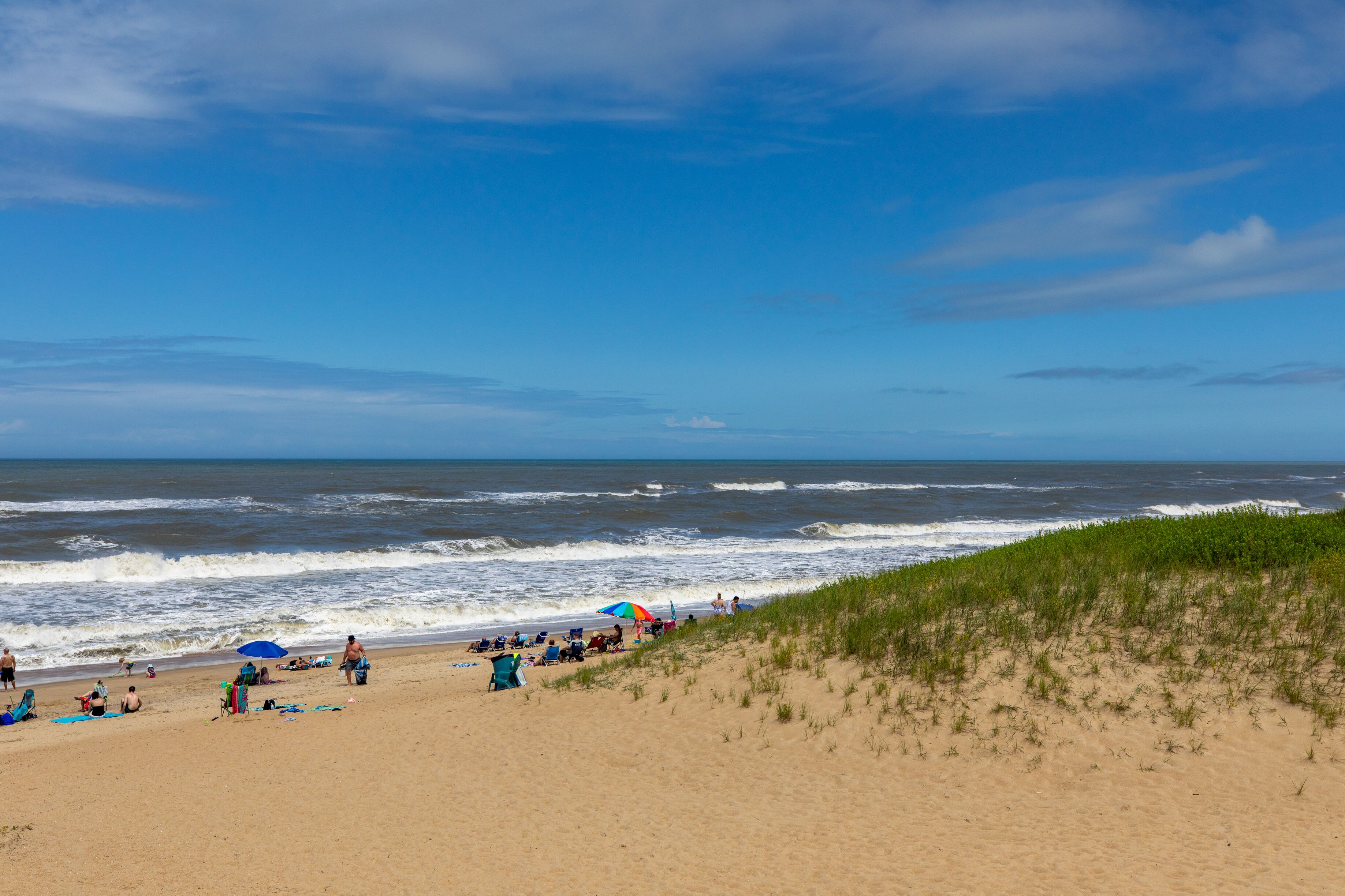 Una playa con gente, sombrillas y dunas.