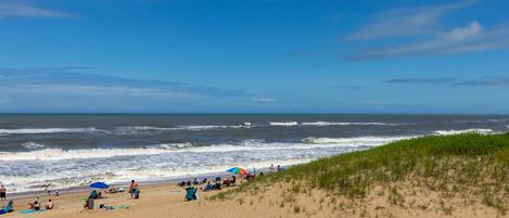 A beach with people, umbrellas, and dunes.