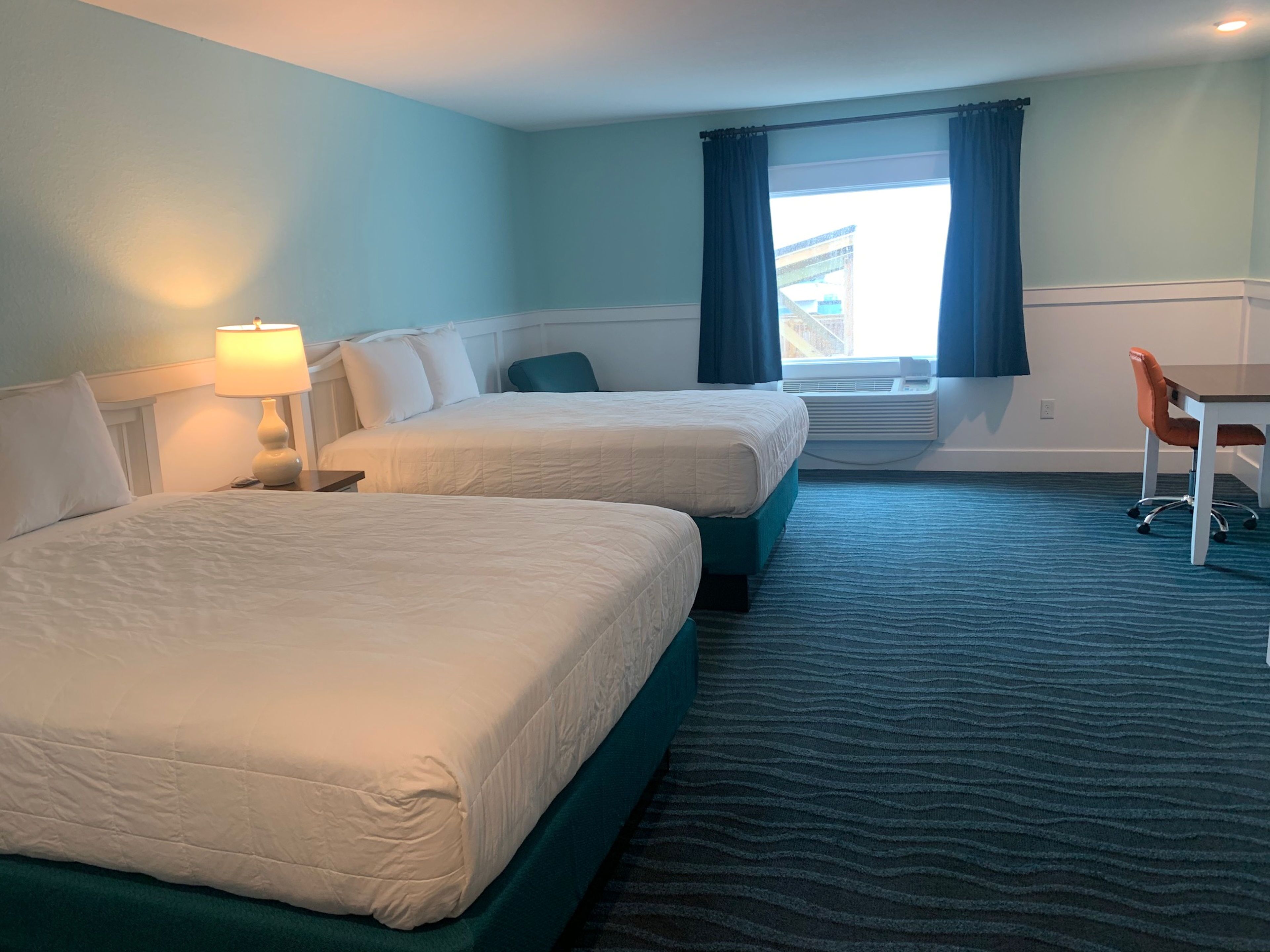 A hotel room with two beds, a desk, a chair, and a window with curtains.