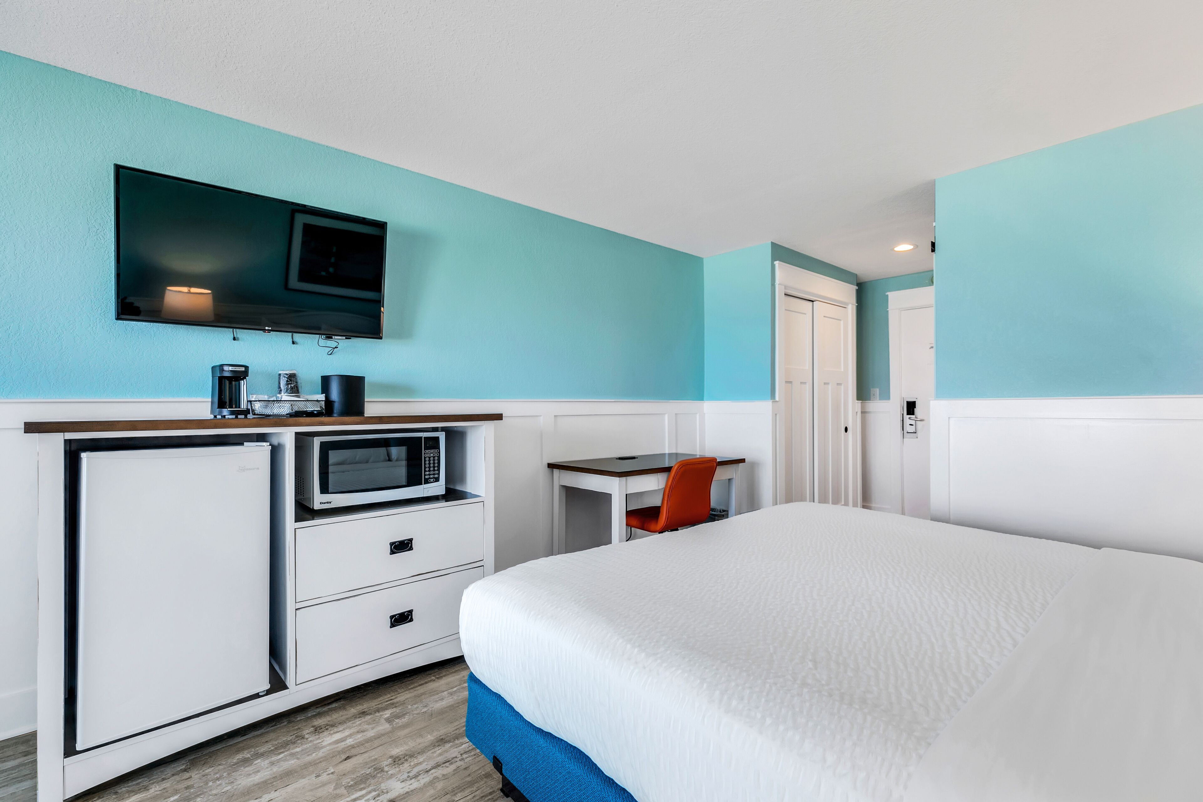 A hotel room with a bed, a desk with a chair, a television, a microwave, and a refrigerator.