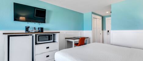 A hotel room with a bed, a desk with a chair, a television, a microwave, and a refrigerator.