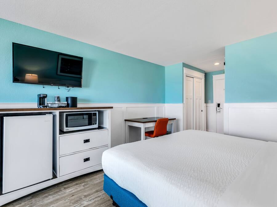A hotel room with a bed, a desk with a chair, a television, a microwave, and a refrigerator.