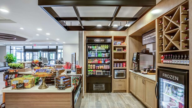 A modern café with a chilled beverage fridge, a frozen section, and a variety of snacks and drinks. - Hilton Garden Inn Boston/Waltham (Waltham)