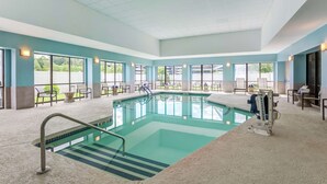 A large indoor swimming pool with clear water, surrounded by lounge chairs and tables, and large windows offering views of the outdoors. - Hilton Garden Inn Boston/Waltham (Waltham)
