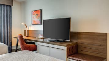 Habitación de hotel con cama, escritorio con televisor de pantalla plana, silla y estante fijado a la pared.