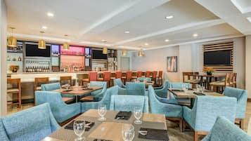 Restaurante com assentos estofados em azul e mesas, área de bar com prateleiras de garrafas e iluminação pendente.