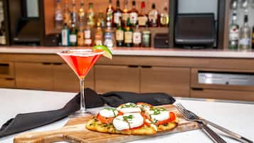 Una copa de martini con un adorno de lima y una tabla de madera con una pizza cubierta de tomates, mozzarella y hierbas.