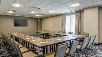 Un salón de conferencias con una larga mesa, sillas, un proyector y una pantalla de televisión.