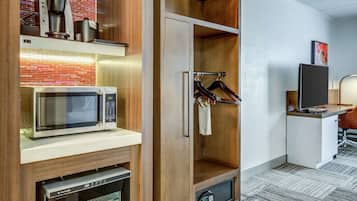 A kitchenette with a microwave, coffee maker, and oven. There is a wooden cabinet with a hanging rack and a television on a stand.