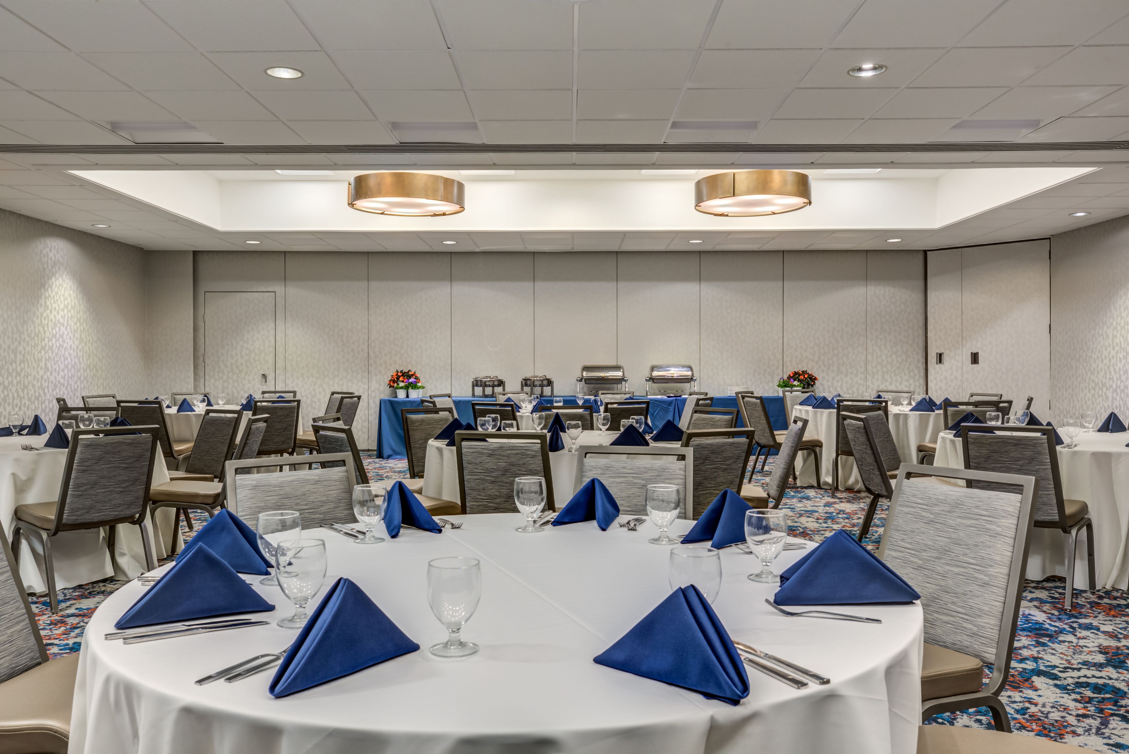 A conference room with round tables, blue napkins, and a patterned carpet.