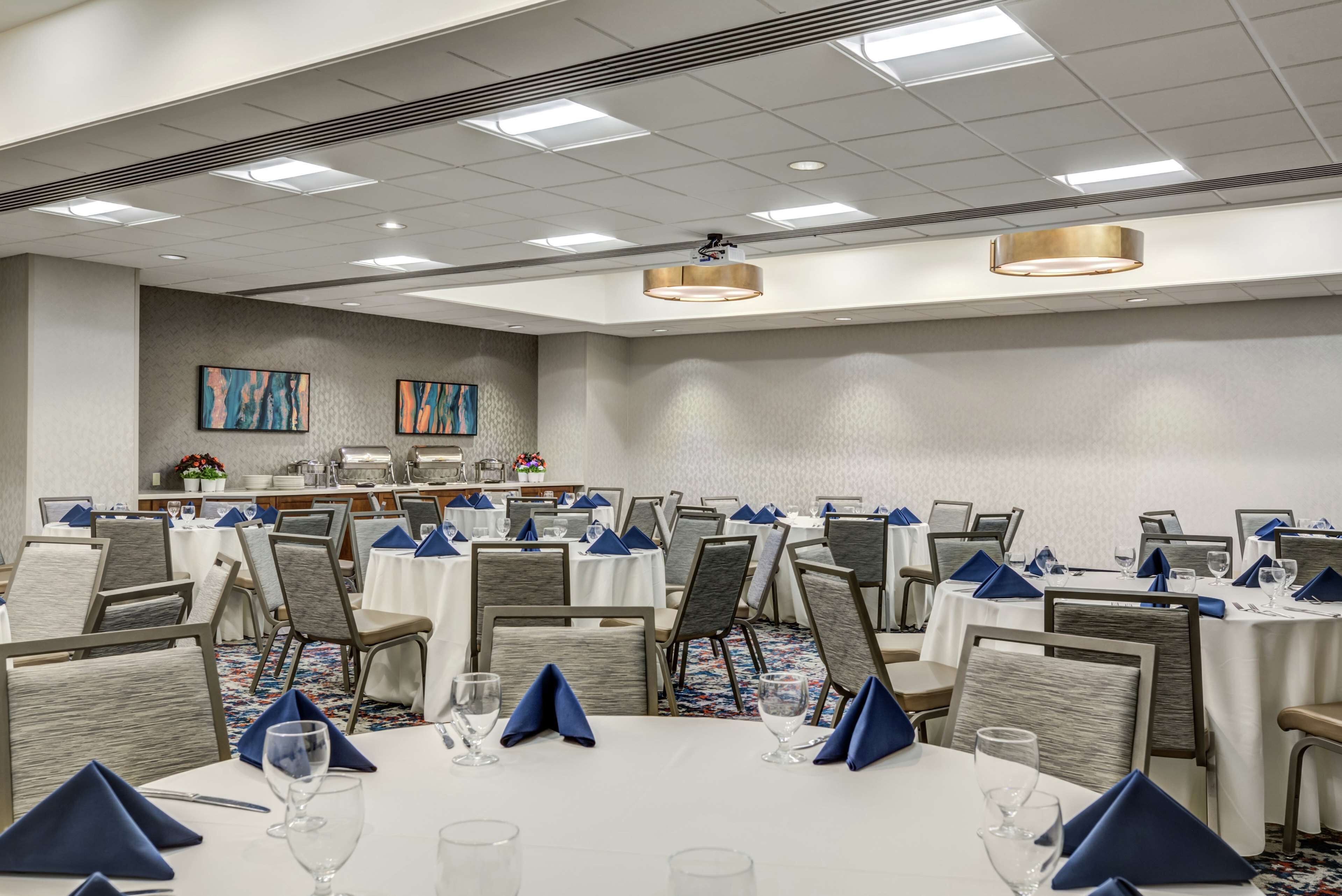 Un salón de conferencias con mesas redondas, sillas y una pantalla para proyector.