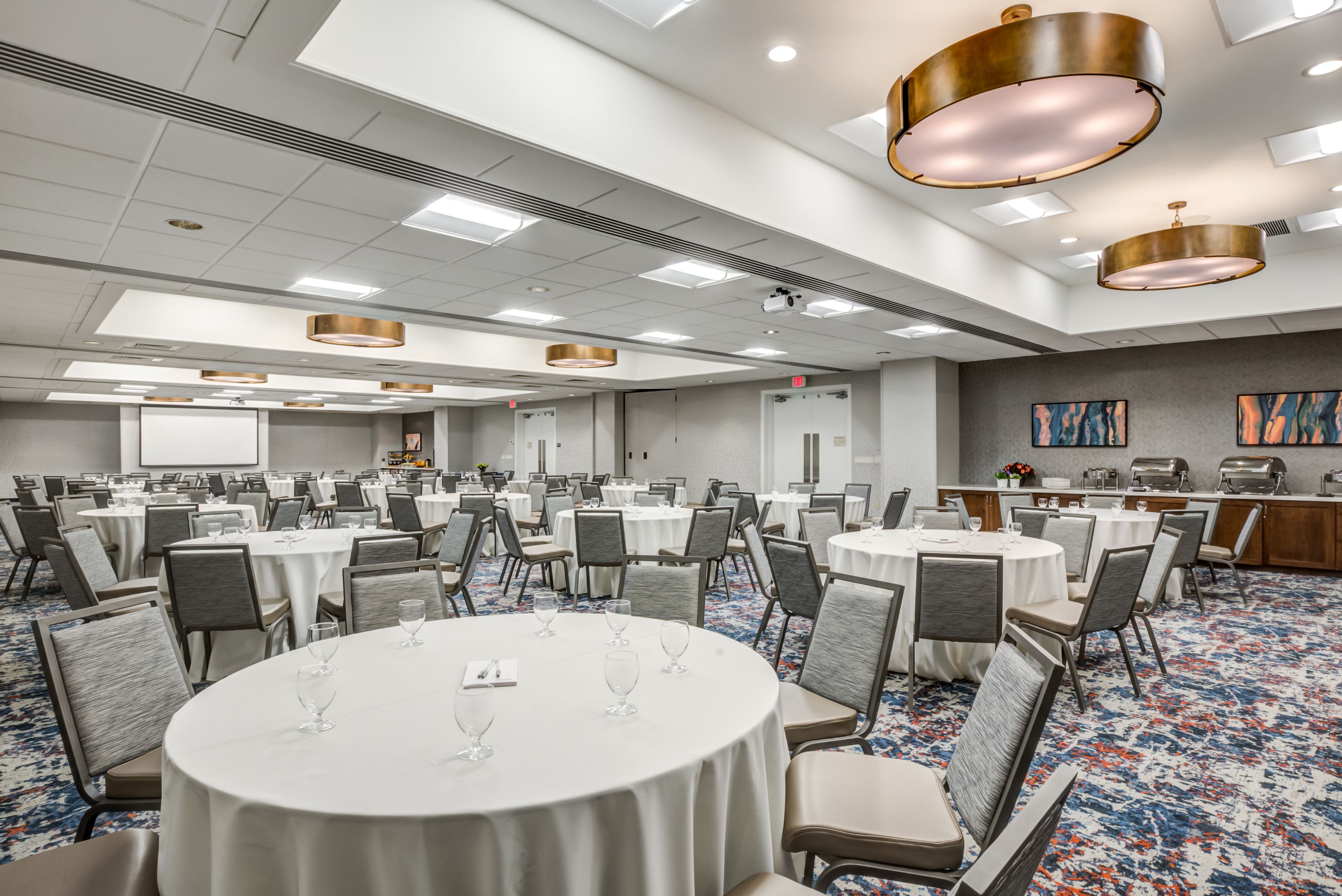 A large conference room with round tables, chairs, and a buffet area.