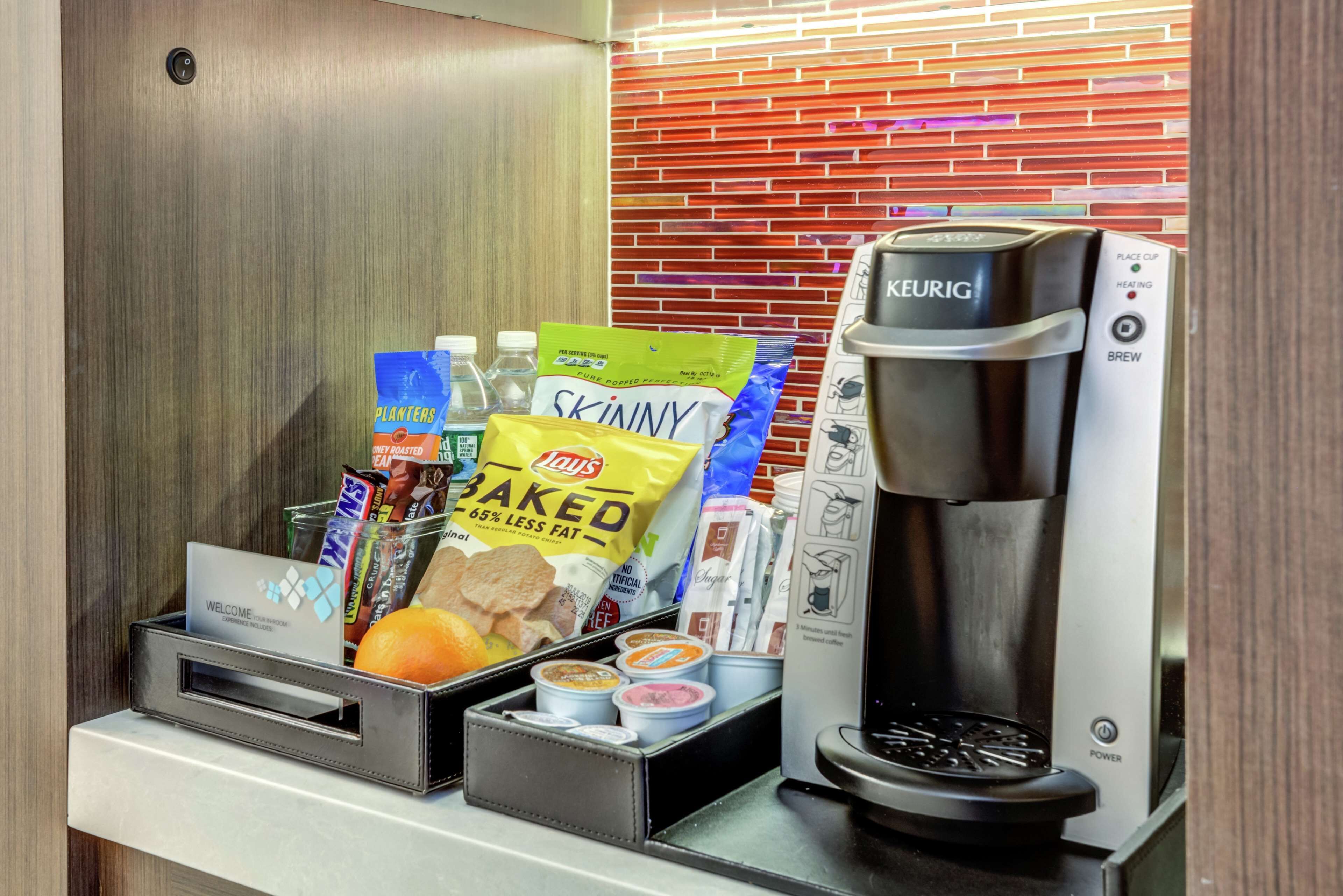 A coffee machine and a snack bar with snacks, drinks, and condiments.