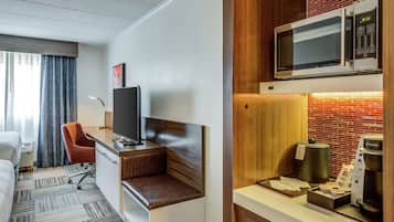 A hotel room with a bed, a desk with a computer, a television, a microwave, a coffee maker, and a small kitchenette.