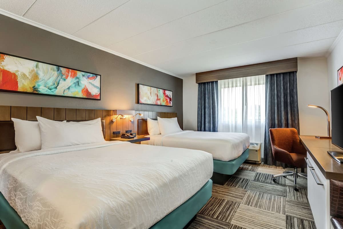 A hotel room with two beds, a desk, a chair, and artwork on the walls.