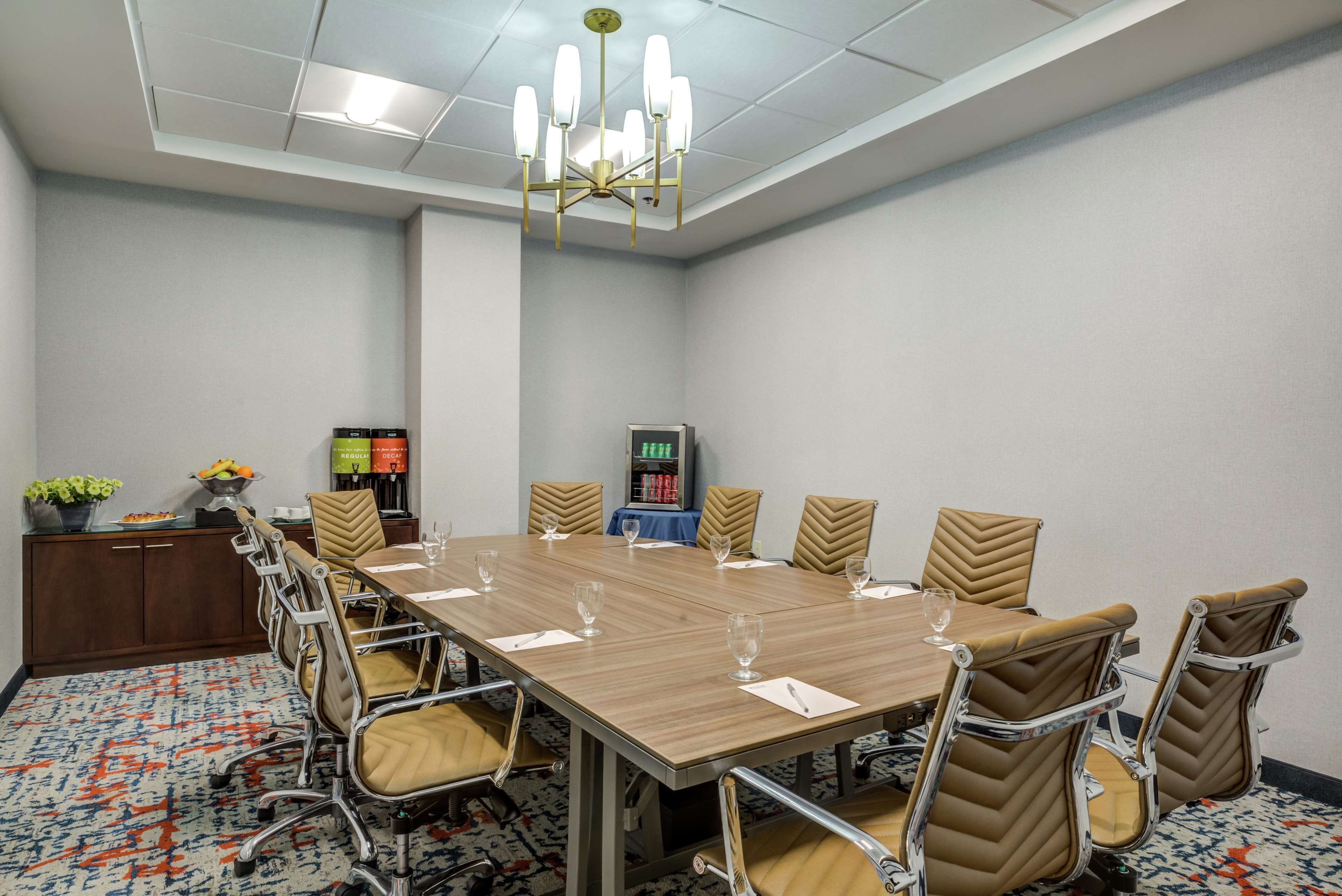 Une salle de conférence avec une longue table, des chaises, un lustre, une horloge et une petite plante placée sur le côté.