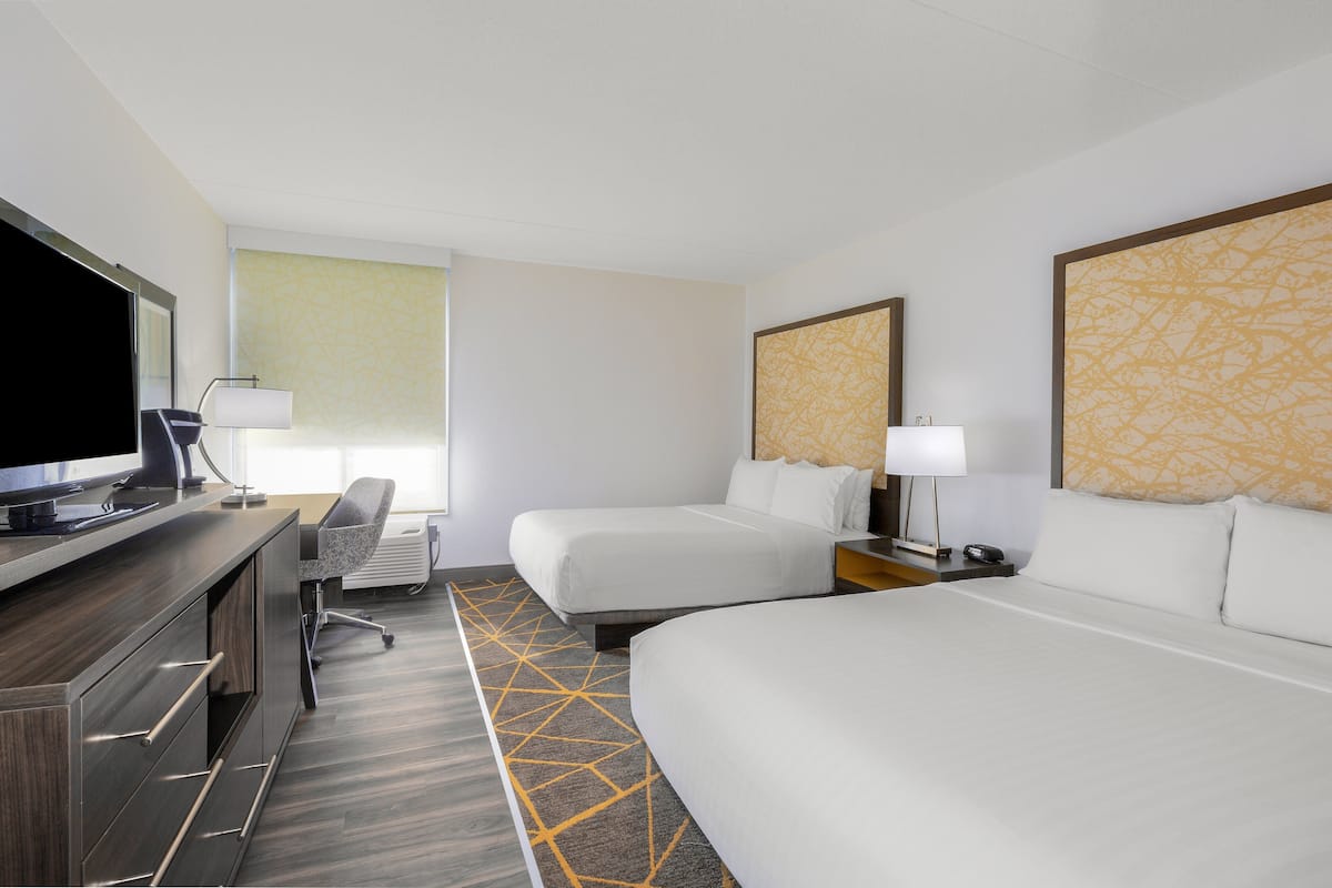 A hotel room with two beds, a desk with a computer, a chair, and a TV.