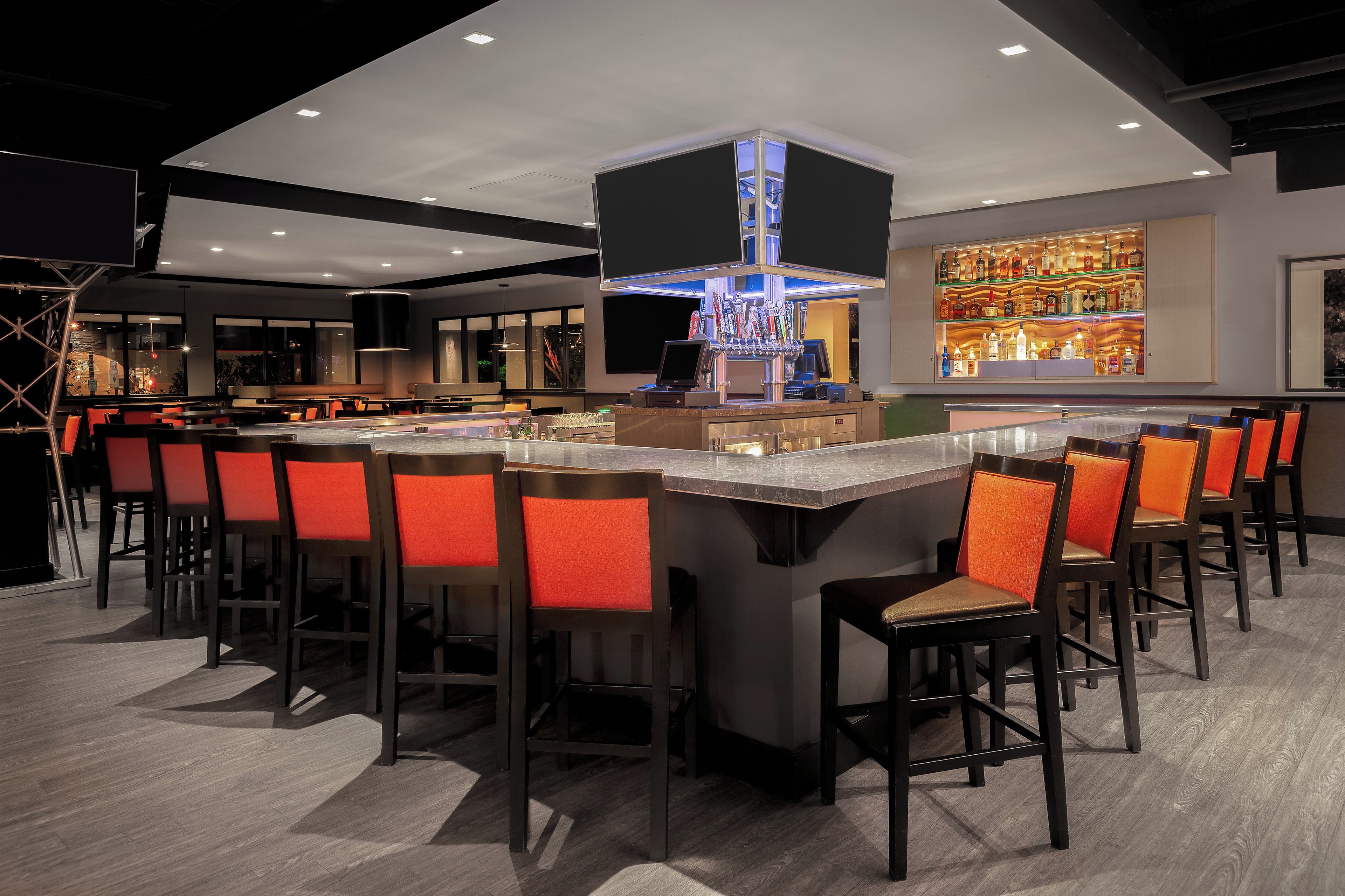 A bar area with a central bar counter, multiple stools, and a well-lit bar with a variety of bottles.