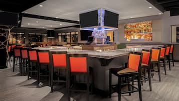 A bar area with a central bar counter, multiple stools, and a well-lit bar with a variety of bottles.