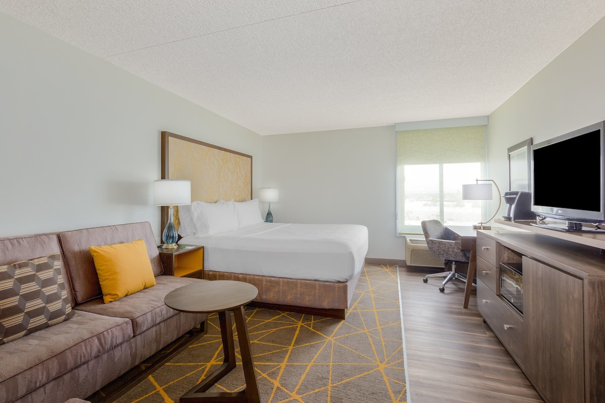 A hotel room with a bed, a sofa, a desk, a television, and a window.