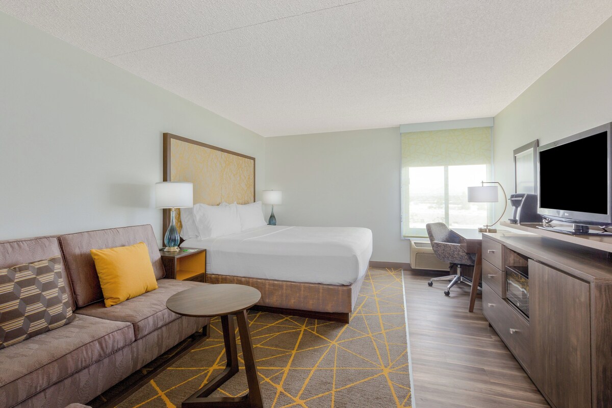 Una habitación de hotel con cama, sofá, escritorio, televisor y ventana.