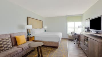 A hotel room with a bed, a sofa, a desk, a television, and a window.