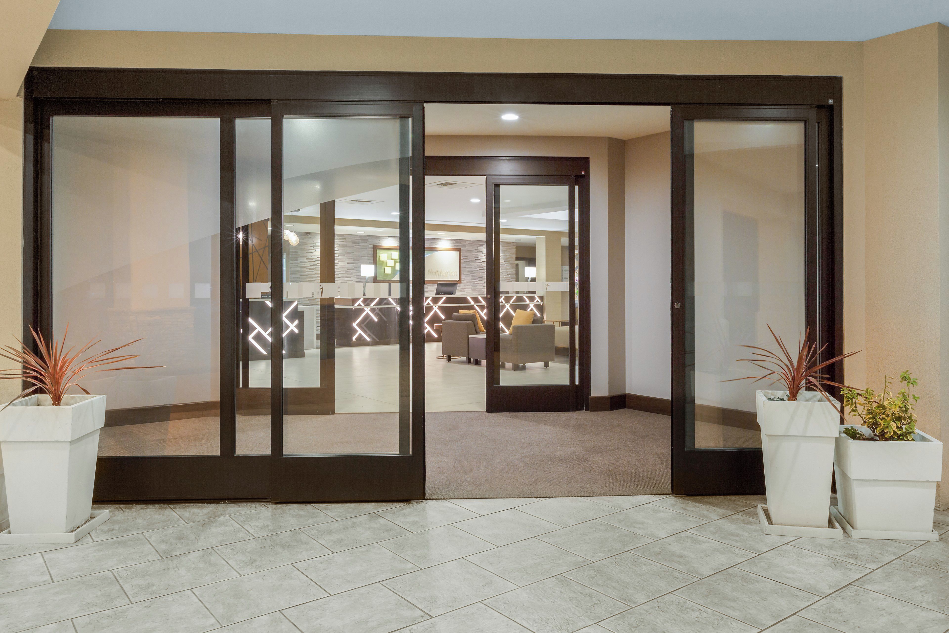 A hotel entrance with a glass door, a reception desk, and a seating area visible through the door.