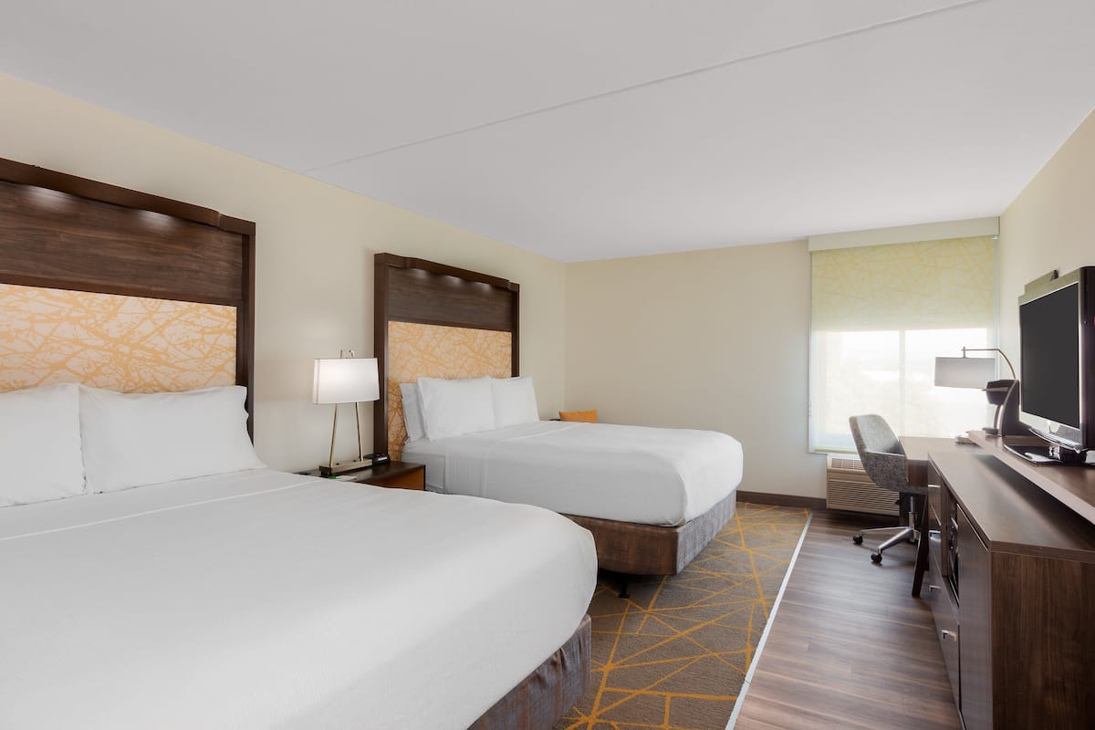 A hotel room with two beds, a desk with a TV, and a window with a view.