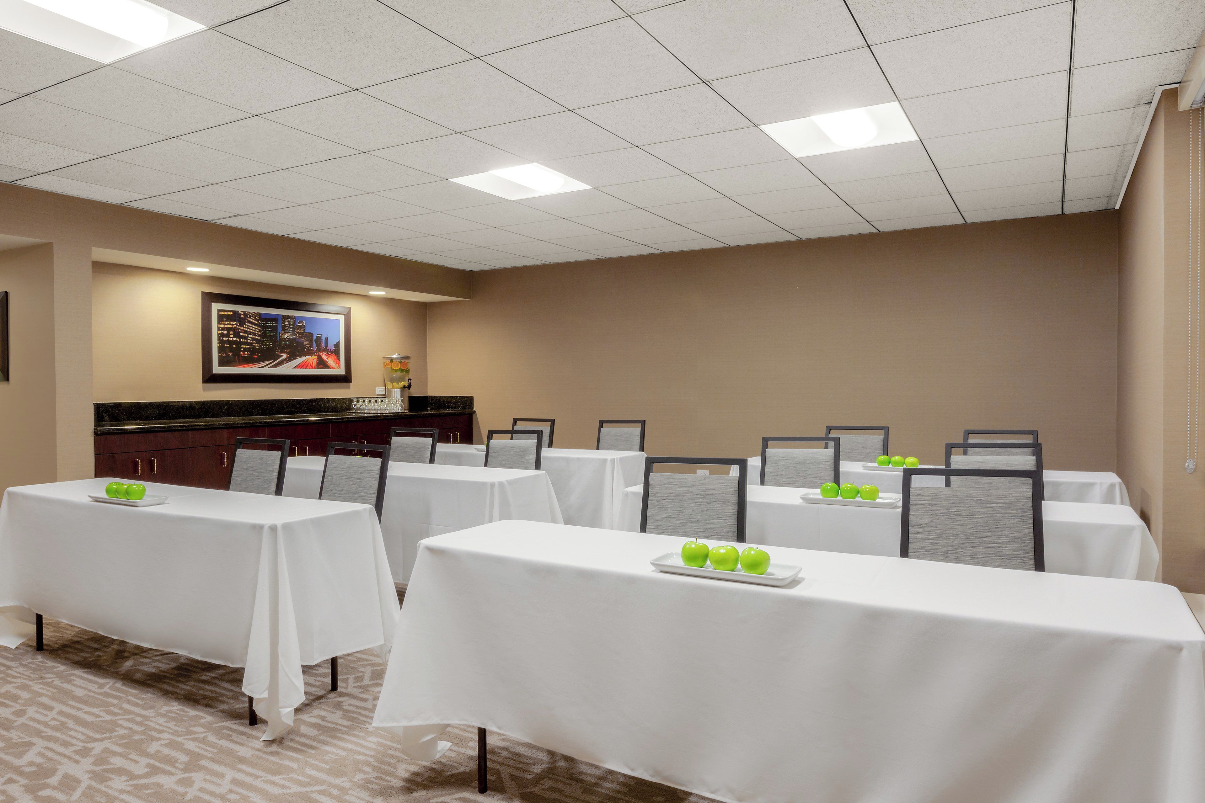 A conference room with multiple tables, each with a white tablecloth and a plate of green apples.