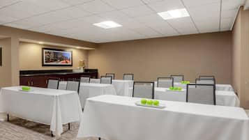 Un salón de conferencias con varias mesas, cada una cubierta con un mantel blanco y un plato de manzanas verdes.