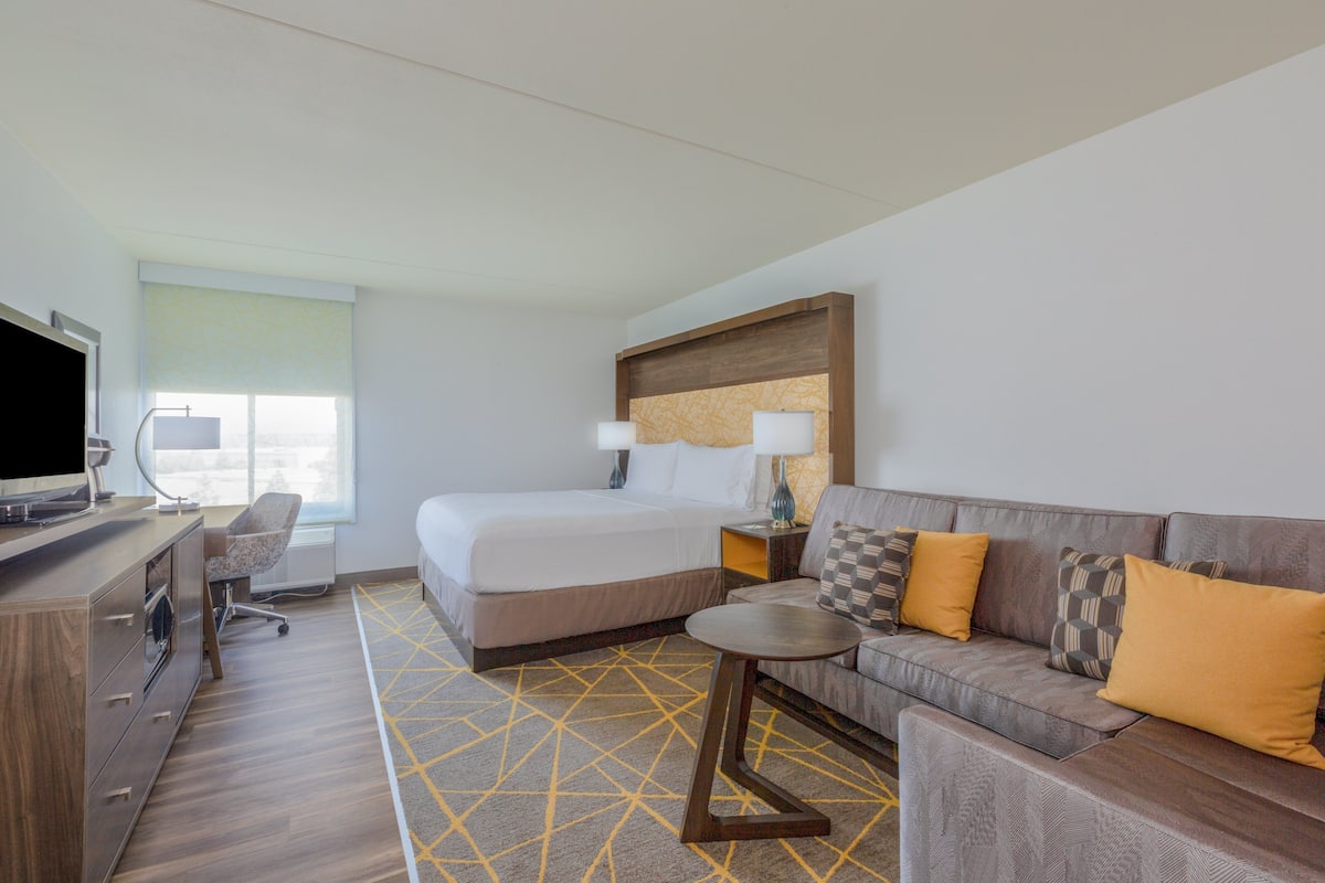 A hotel room with a bed, a sofa, a TV, a desk, and a lamp.
