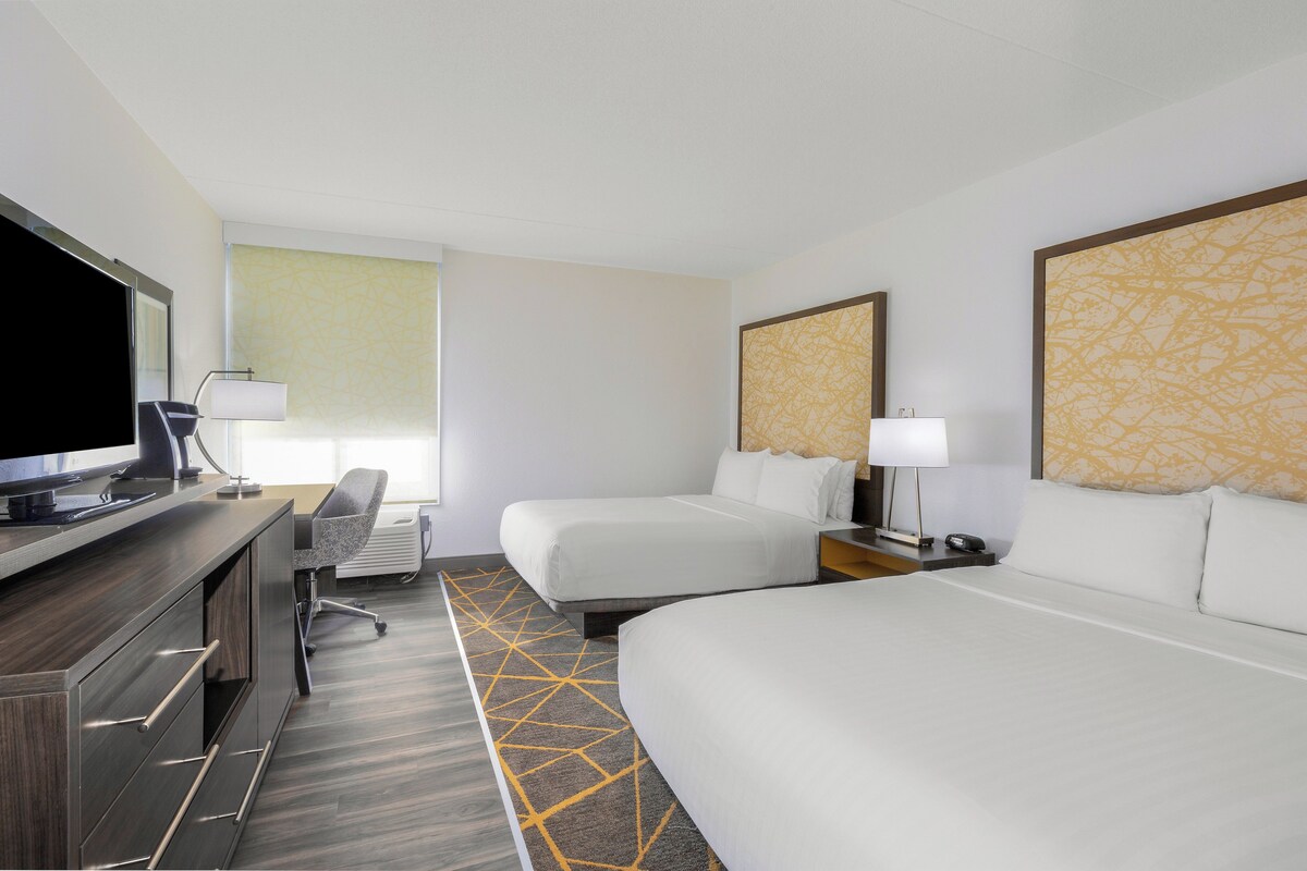 Una habitación de hotel con una cama, un escritorio con televisor, una silla y una lámpara.
