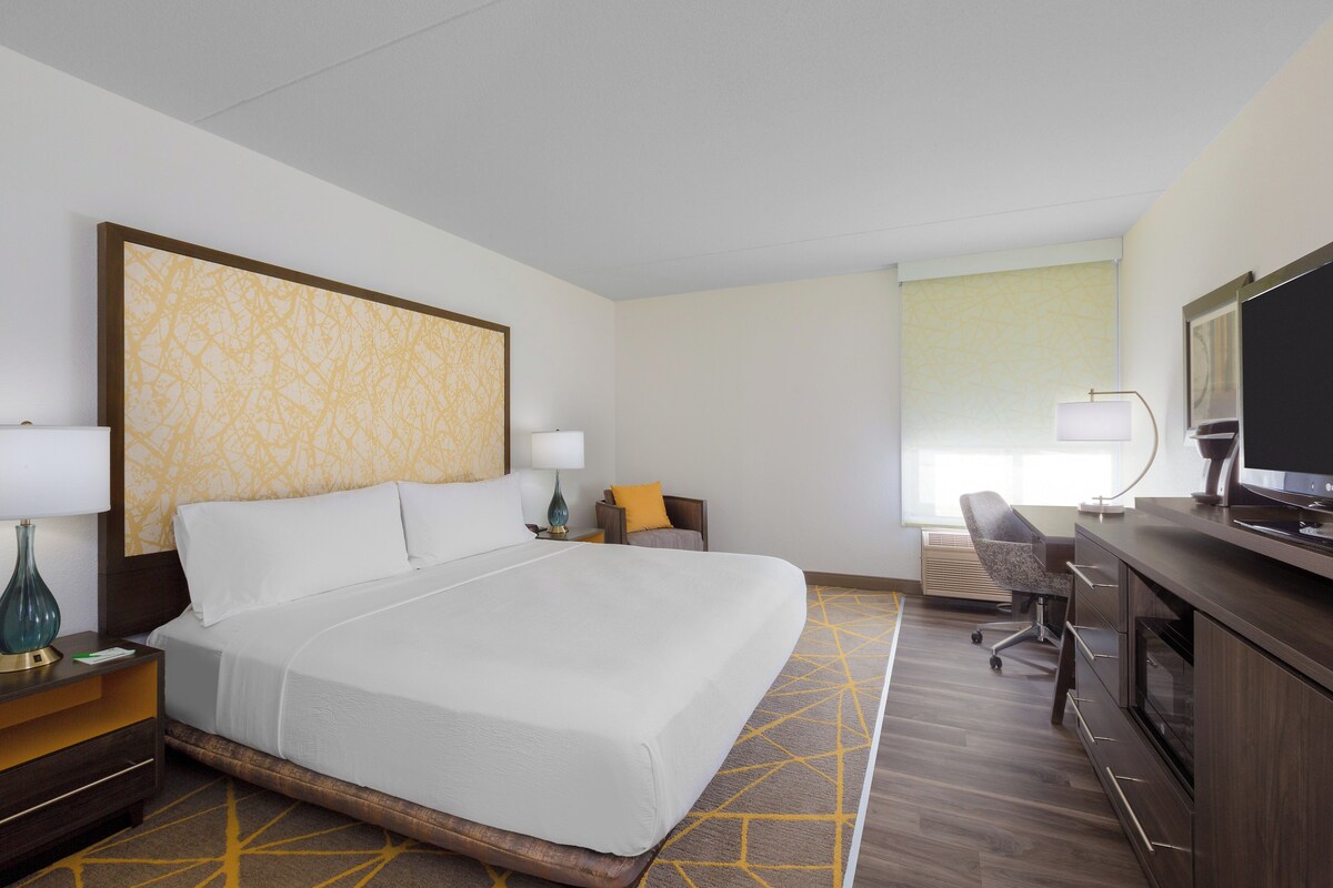 Habitación de hotel con una cama grande, un escritorio con silla, televisión y ventana.