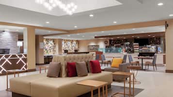 Un moderno vestíbulo de hotel con zona de estar, mostrador de recepción y bar.