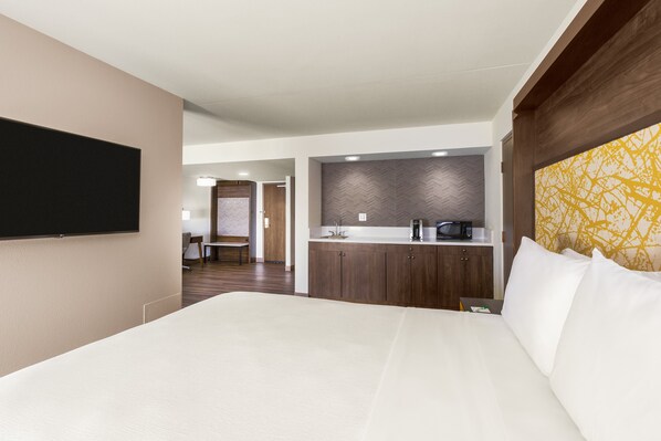 Habitación de hotel con una cama grande, un televisor de pantalla plana montado en la pared, una kitchenette con microondas y un revestimiento de pared con patrón de espiga.
