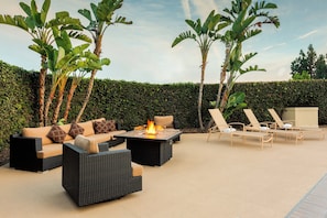 An outdoor seating area with a fire feature, lounge chairs, and a hedge backdrop. - Holiday Inn La Mirada – Buena Park by IHG (La Mirada)