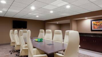 A conference room with a large table, multiple chairs, a flat-screen TV, and a framed artwork on the wall.