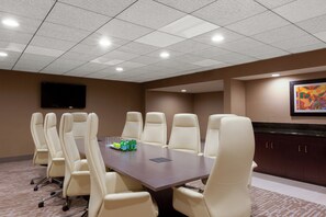 A conference room with a large table, multiple chairs, a flat-screen TV, and a framed artwork on the wall.