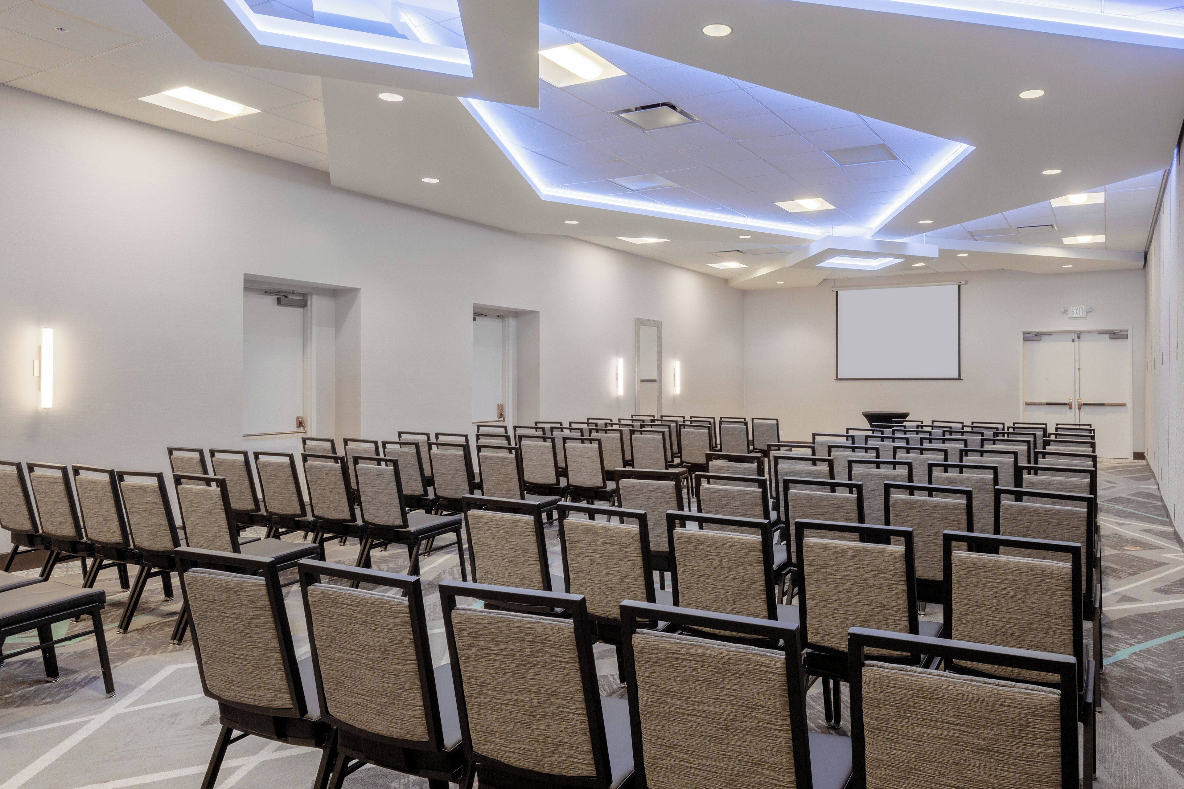 A conference room with rows of chairs, a projector screen, and a whiteboard.