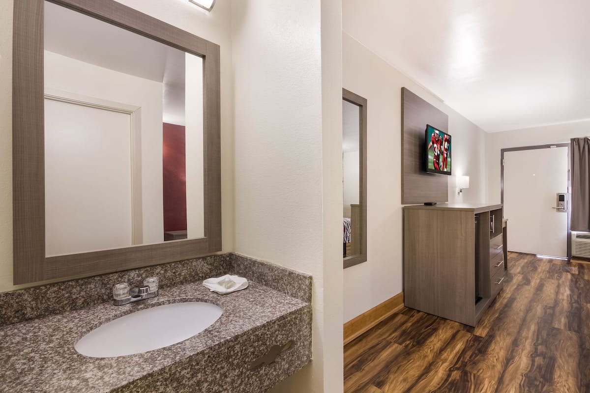 Un baño de hotel con lavamanos de encimera de granito, un espejo grande y un mueble de tocador de madera.