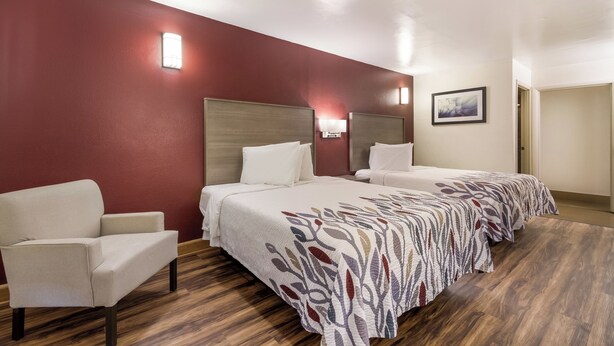 A hotel room with a large bed, a chair, and a painting on the wall. - Red Roof Inn Crestview (Crestview)