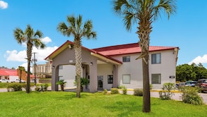 A two-story building with a red roof, surrounded by well-maintained grass and palm trees. - Red Roof Inn Crestview (Crestview)