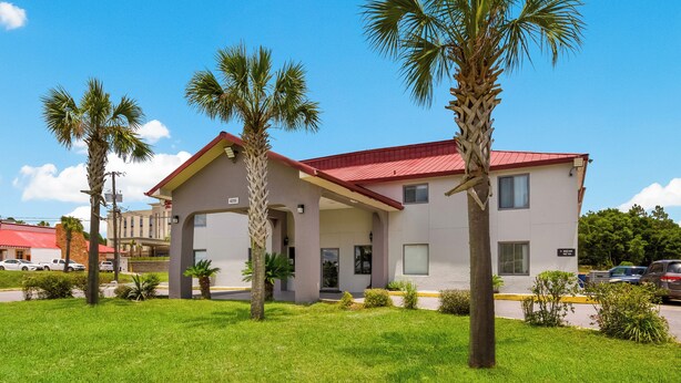 A two-story building with a red roof, surrounded by well-maintained grass and palm trees. - Red Roof Inn Crestview (Crestview)