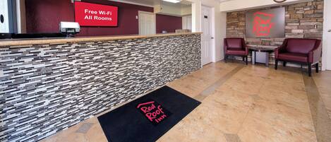 Een hotel receptie met een modern design, met een receptiebalie, een digitaal scherm dat gratis Wi-Fi promoot en een Red Roof Inn bord.