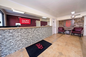 A hotel reception area with a modern design, including a reception desk, a digital screen advertising free Wi-Fi, and a Red Roof Inn sign. - Red Roof Inn Crestview (Crestview)
