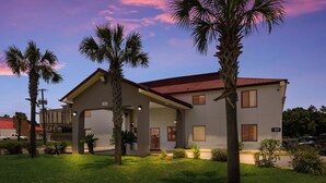 A two-story house with a red roof, a covered porch, and a well-maintained lawn with palm trees. - Red Roof Inn Crestview (Crestview)