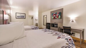 A hotel room with two beds, a TV mounted on the wall, a desk with a chair, and a small table with a lamp. - Red Roof Inn Crestview (Crestview)
