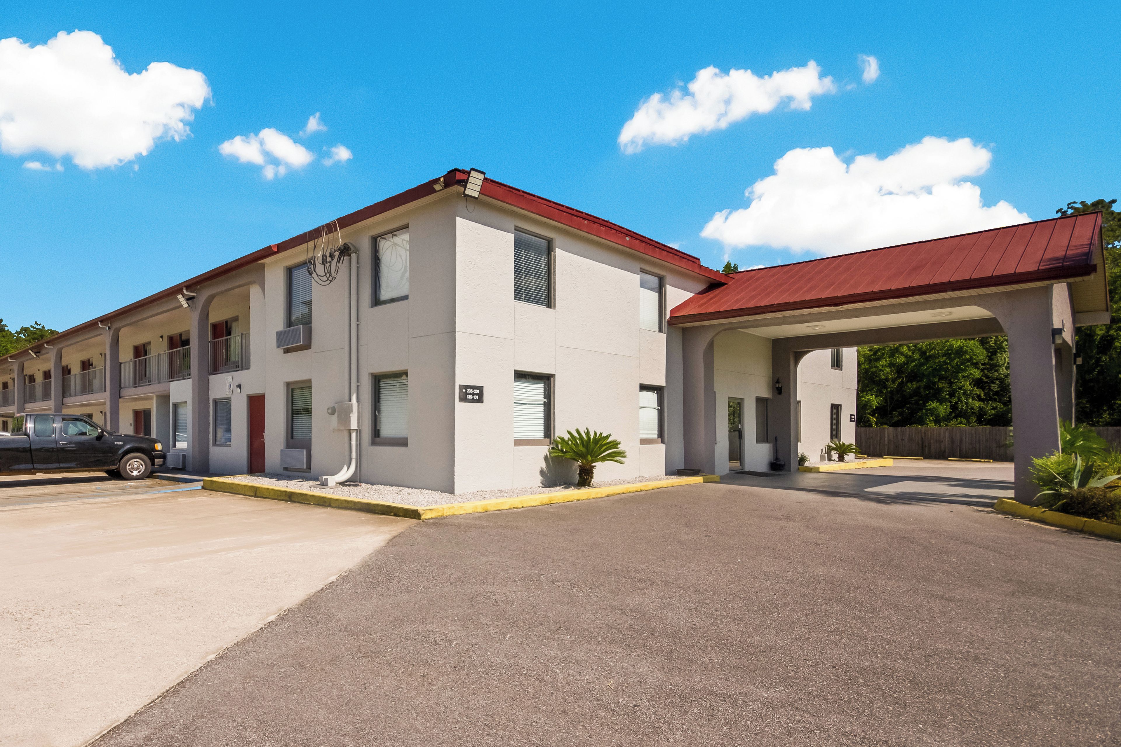A multi-story motel with a red roof, a covered parking area, and a clear blue sky.