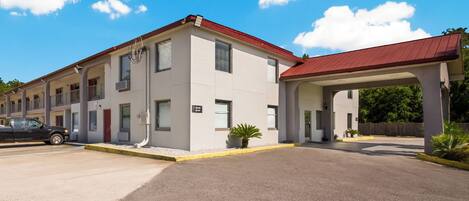 A multi-story motel with a red roof, a covered parking area, and a clear blue sky.
